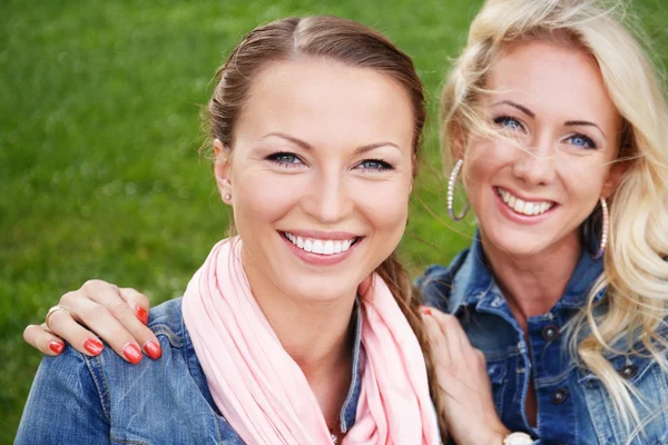 2 つの美しい若い女性、公園のベンチに座っているジーンズのジャケットに笑みを浮かべて — ストック写真