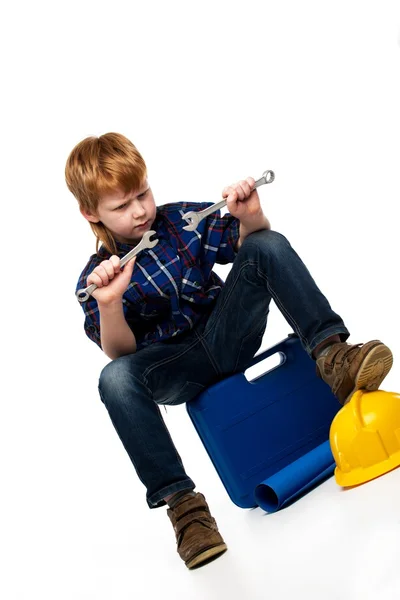 Verveeld mechanic jongetje met moersleutel tools zittend op een werkset — Stockfoto