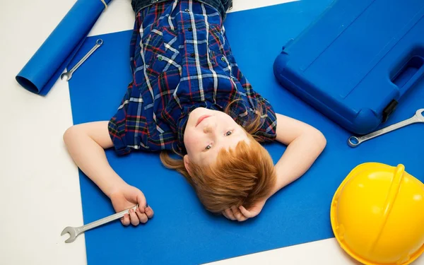 Funny little mechanic boy with wrench tools lying on a blueprint — Stock Photo, Image