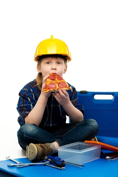 Маленький забавный механик ест пиццу среди инструментов — стоковое фото