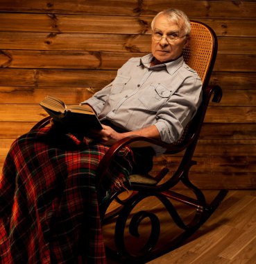 Senior man sitting in rocking chair in homely wooden interior with old book clipart