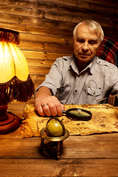 Homem sênior com lupa olhando para o mapa do vintage em interior de madeira caseira — Fotografia de Stock