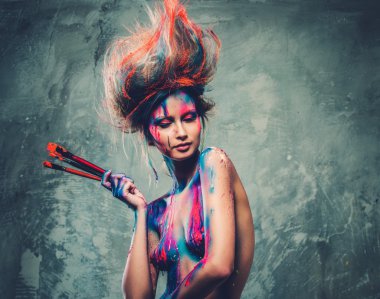 Young woman muse with creative body art and hairdo holding paint brushes  clipart