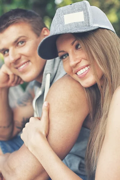 Junges fröhlich lächelndes sportliches Paar sitzt auf Bank im Park — Stockfoto