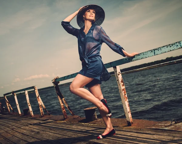 Stijlvolle vrouw in witte hoed staande op oude houten pier — Stockfoto