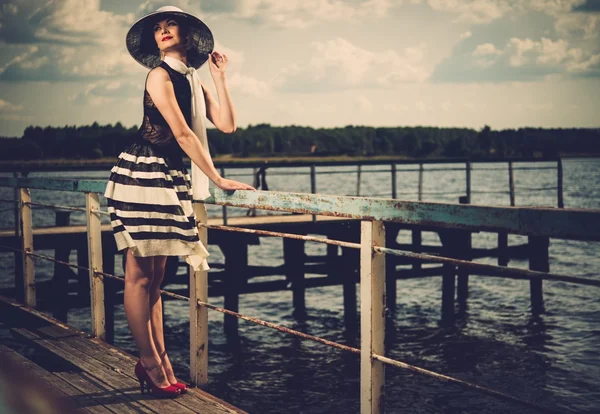 Mujer en sombrero blanco y bufanda de pie cerca de viejos rieles del muelle — Foto de Stock