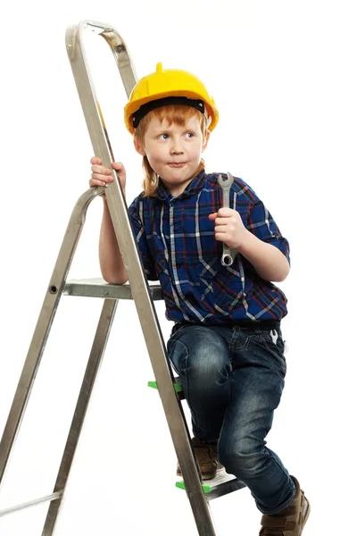 Malý chlapec v ochranné přilbě nástrojem klíč na žebříku — Stock fotografie