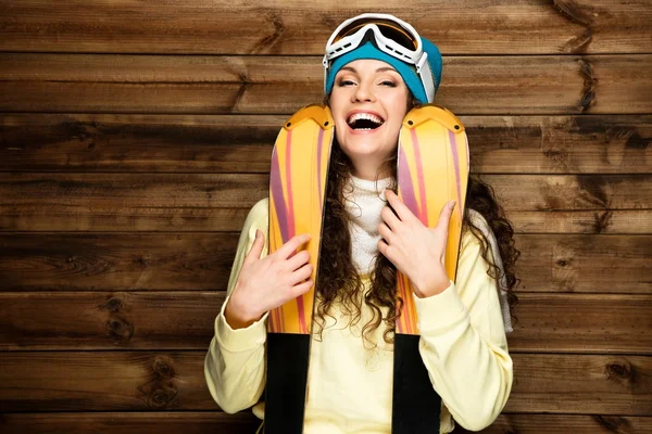 Lachende vrouw met ski's permanent tegen houten huis muur — Stockfoto