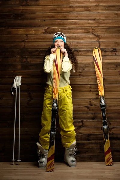 Mulher feliz com esquis e botas de esqui perto de parede de madeira — Fotografia de Stock