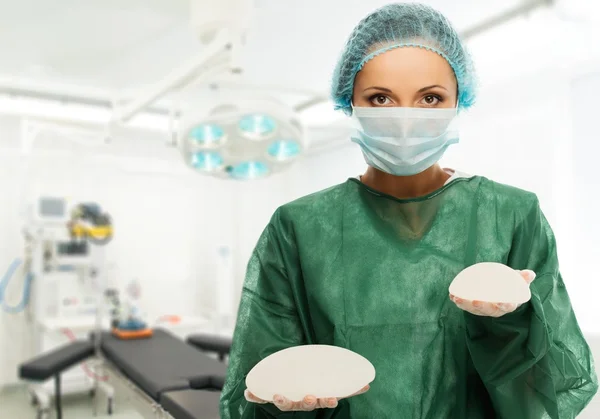 Cirurgião plástico mulher segurando diferentes tamanhos de silicone implantes mamários na sala de cirurgia interior — Fotografia de Stock