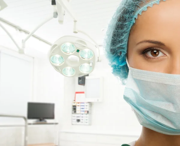 Young woman doctor in cap and face mask in surgery room interior — Stock Photo, Image