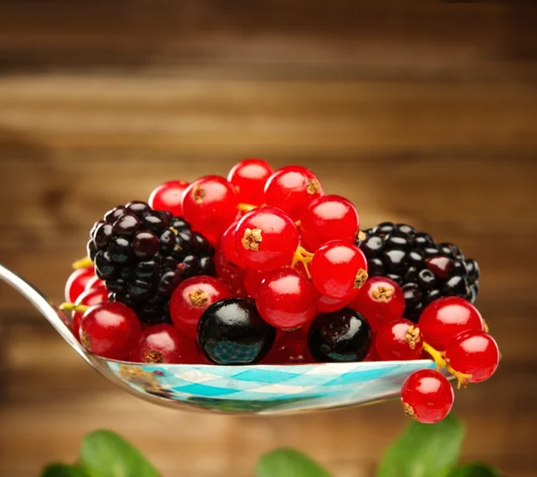 Fresh berries on a spoon against wooden background — Stock Photo, Image