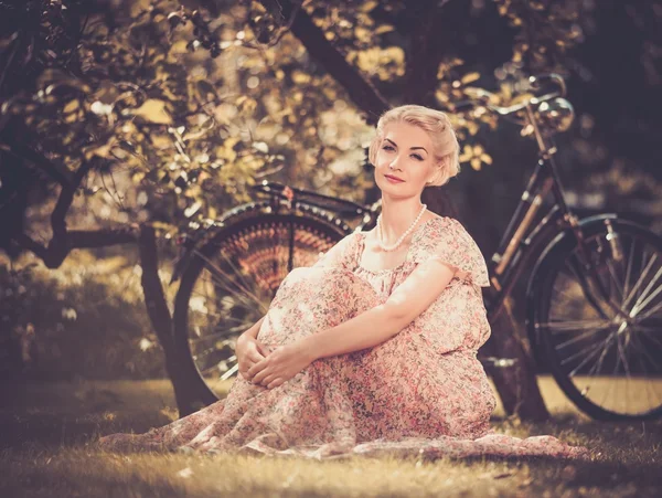 Dreaming blond retro woman in summer dress sitting on a meadow — Zdjęcie stockowe