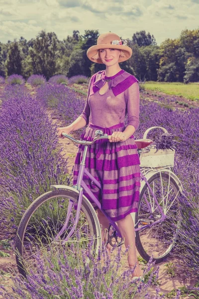 ラベンダー畑でレトロな自転車と紫色のドレスと帽子の女 — ストック写真