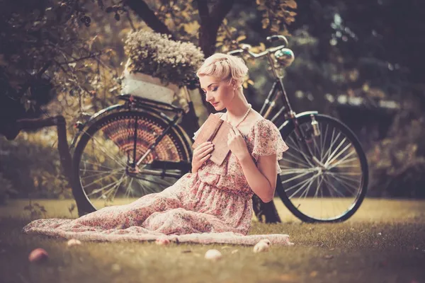 Femme rétro blonde rêveuse avec un livre en robe d'été assis sur une prairie — Photo