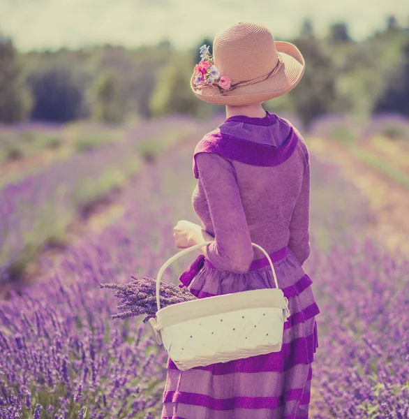 Mulher de vestido roxo e chapéu com cesta no campo de lavanda — Fotografia de Stock
