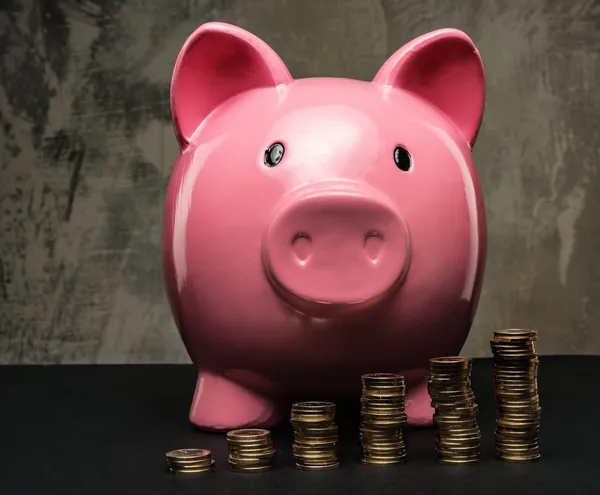 Pilhas de moedas em frente ao banco dos porquinhos — Fotografia de Stock