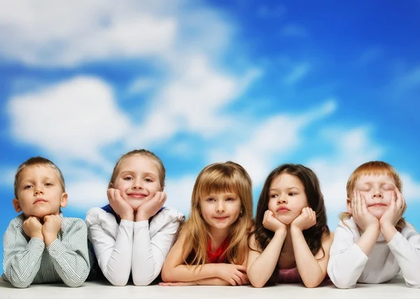 Grupo de niños pequeños acostados en fila contra el cielo azul —  Fotos de Stock