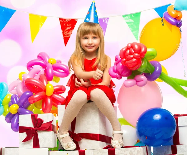 Kleines Mädchen im roten Kleid sitzt auf Geschenkschachteln — Stockfoto
