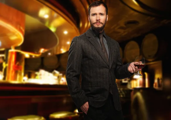 Красивый хорошо одетый мужчина в пиджаке со стаканом напитка в интерьере ресторана — стоковое фото