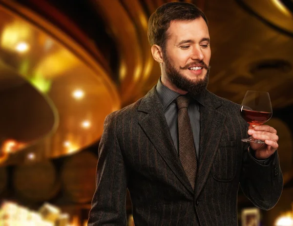 Handsome well-dressed man in jacket with glass of beverage in restaurant interior — Stock Photo, Image