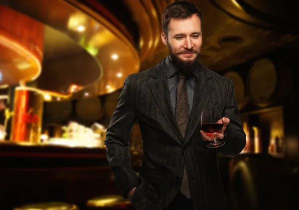 Handsome well-dressed man in jacket with glass of beverage in restaurant interior — Stock Photo, Image