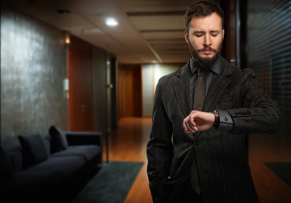 Bello uomo ben vestito con la barba guardando il suo orologio da polso in un corridoio — Foto Stock
