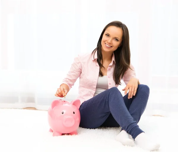 Cheerful young woman sitting on a carpet with piggybank — Stock Photo, Image