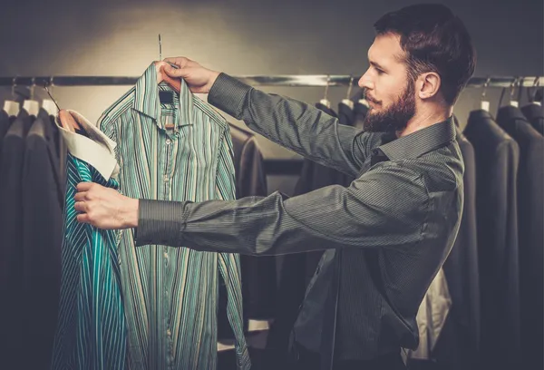 Knappe man met baard kiezen shirt in een winkel — Stockfoto
