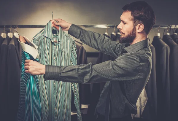 Hombre guapo con barba escogiendo camisa en una tienda —  Fotos de Stock