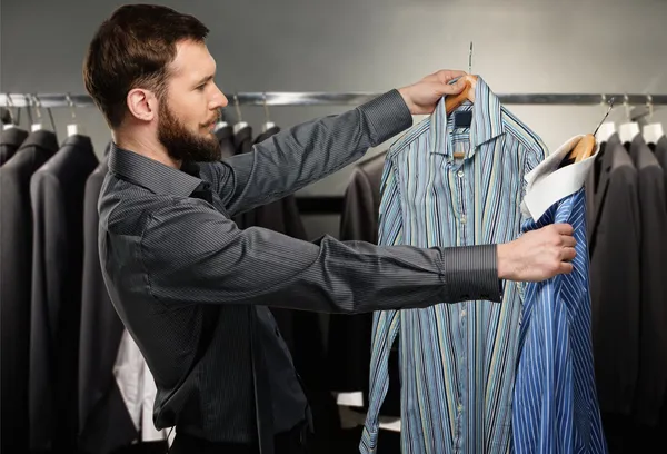 Hombre guapo con barba escogiendo camisa en una tienda — Foto de Stock