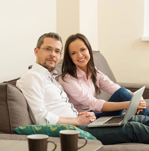 Young cheerful couple with laptop on a sofa in home interior — Stock Photo, Image