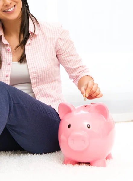 Cheerful young woman sitting on a carpet with piggybank — Stock Photo, Image