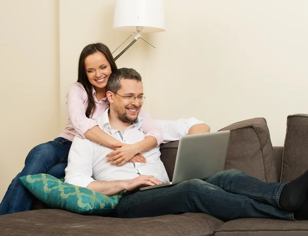 Jovem casal alegre com laptop em um sofá no interior da casa — Fotografia de Stock