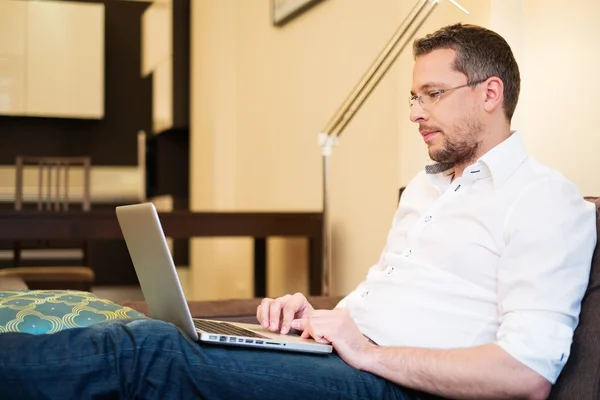 Ung man med grått hår med laptop på soffan i heminredning — Stockfoto