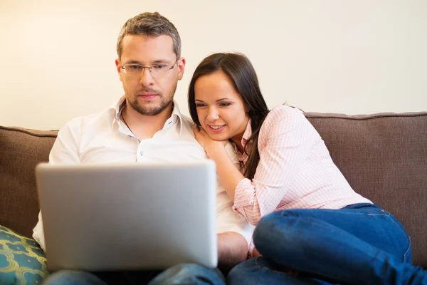 Jovem casal alegre com laptop em um sofá no interior da casa — Fotografia de Stock