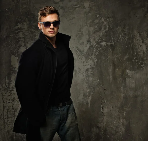 Stijlvolle jonge man in zwarte jas en zonnebril — Stockfoto