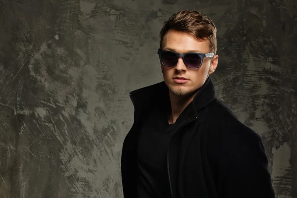 Stylischer junger Mann in schwarzem Mantel und Sonnenbrille — Stockfoto