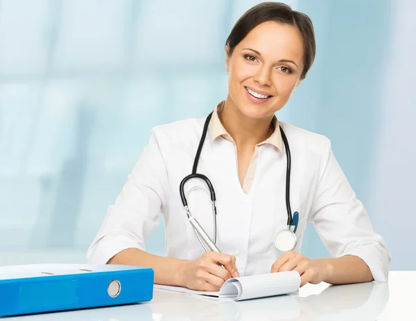 Jeune femme médecin brune positive derrière la table prenant des notes — Photo