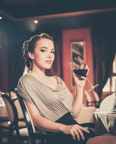 Menina bonita com copo de vinho tinto sozinho em um restaurante — Fotografia de Stock