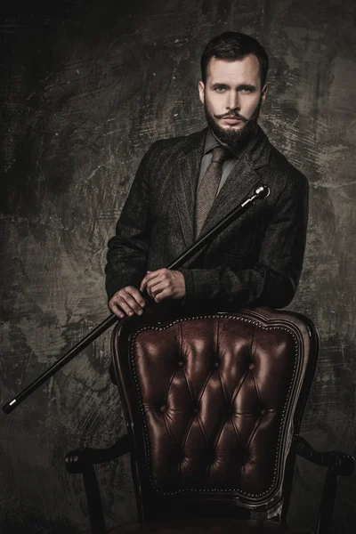 Handsome well-dressed man with stick standing near leather chair — Stock Photo, Image