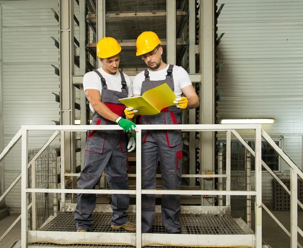 Two positive workers  in safety hats on a factory — Stock Photo, Image