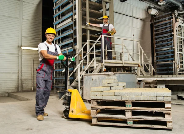 Jovem trabalhador movendo pedras de pavimentação com caminhão de paletes em uma fábrica — Fotografia de Stock