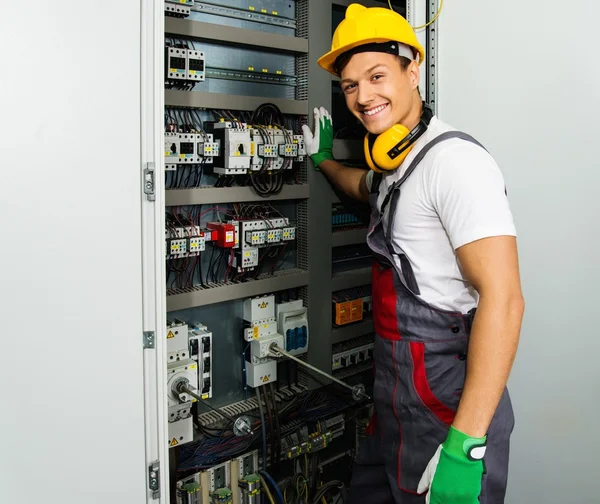 Fröhlicher Elektriker mit Schutzhut in einer Fabrik — Stockfoto