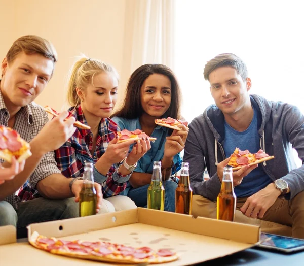 Grupo de jovens amigos multi étnicos com pizza e garrafas de bebida comemorando em casa interior — Fotografia de Stock