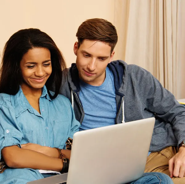 Jóvenes estudiantes multiétnicos pareja con ordenador portátil en el interior del hogar —  Fotos de Stock