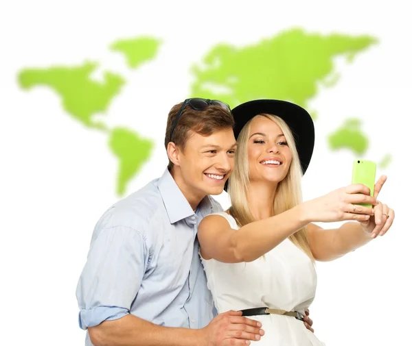 Beautiful smiling young couple making selfie against world map — Stock Photo, Image