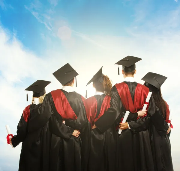 Groep afgestudeerd jonge studenten in zwarte mantels tegen blauwe hemel — Stockfoto