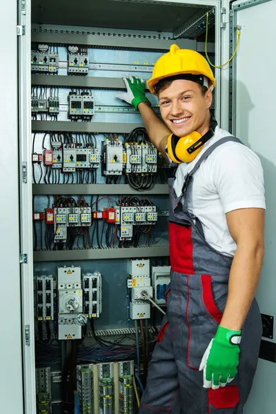 Fröhlicher Elektriker mit Schutzhut in einer Fabrik — Stockfoto