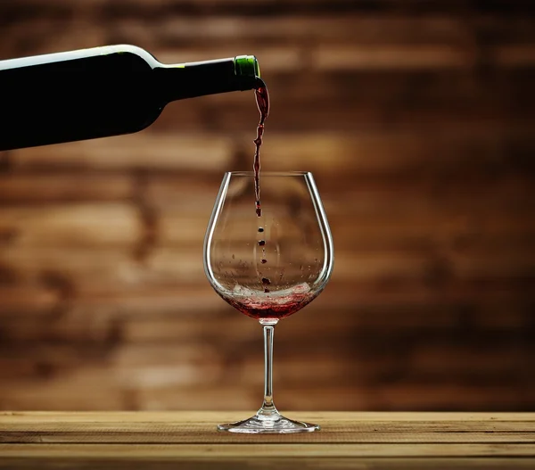 Pouring red wine into the glass against wooden background — Stock Photo, Image